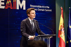 De minister staat aan een spreekstoel.