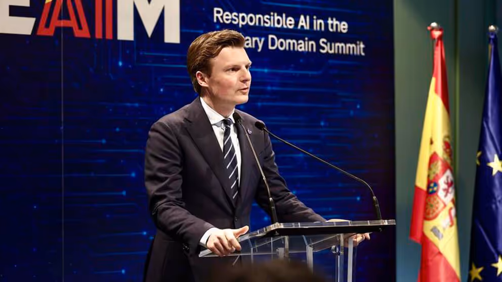 De minister staat aan een spreekstoel.