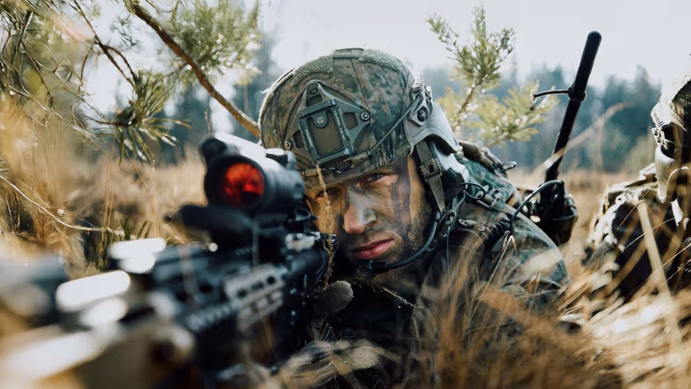 Een militair in de bosjes kijkt door een wapen.