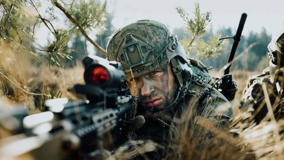 Een militair in de bosjes kijkt door een wapen.