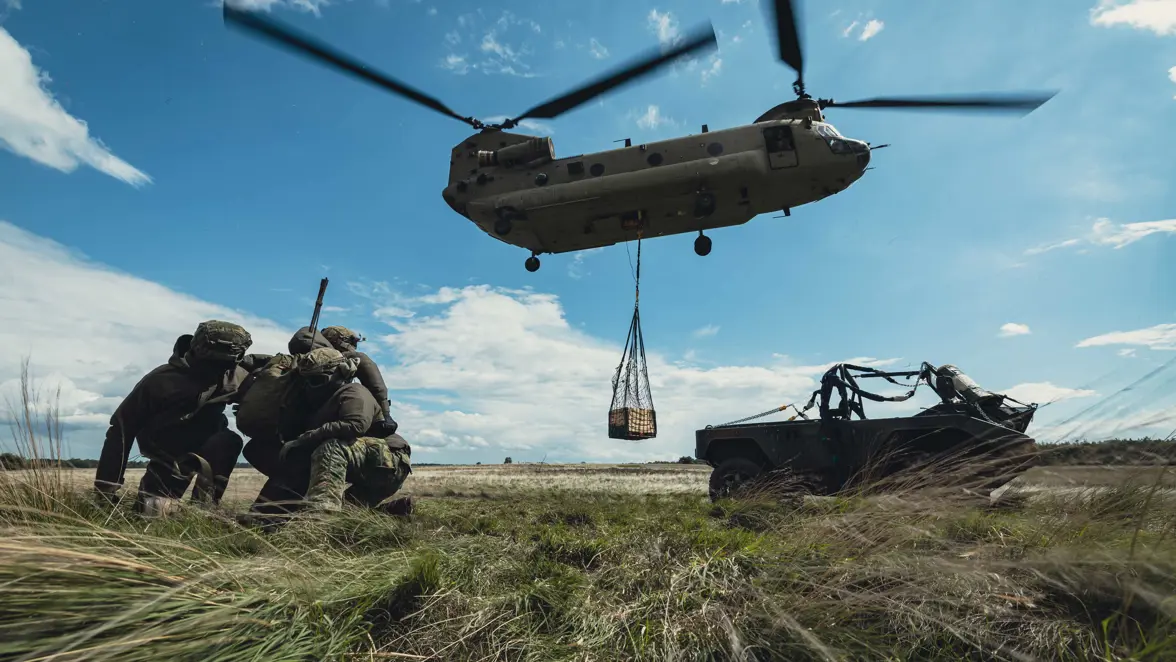 Drie militairen houden elkaar vast. Naast hen staat een voertuig geparkeerd, klaar voor transport.