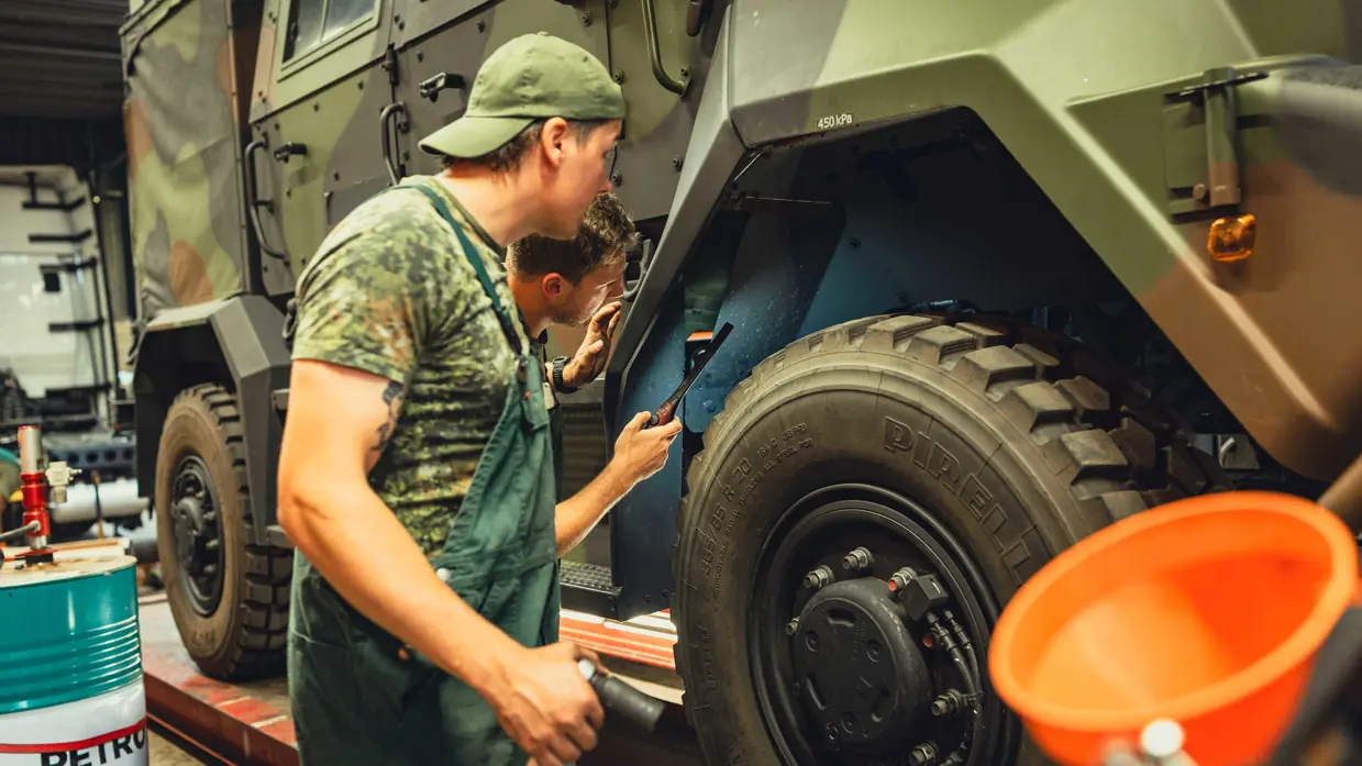 Twee militairen in groene overall kijken met een lampje in de wielkast van de militaire Manticore.