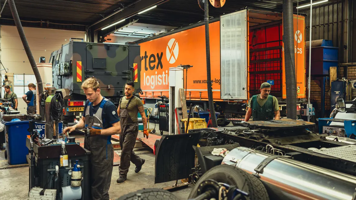 We kijken naar de werkplaats van Iveco Schouten te Nijmegen. Militairen in groene overalls sleutelen er, samen met burgermedewerkers, aan civiele vrachtwagens en militaire voertuigen.