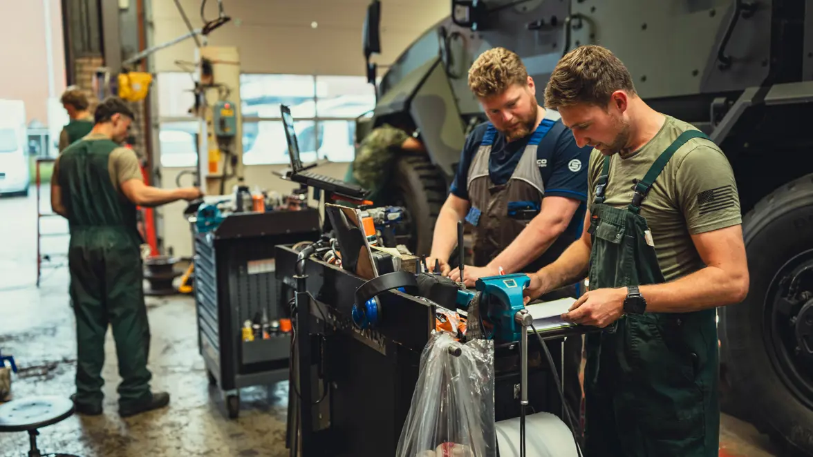 Een burgermedewerker van Iveco en een militair kijken naar een computerscherm. Achter hen is de Manticore op de werkplaats te zien.