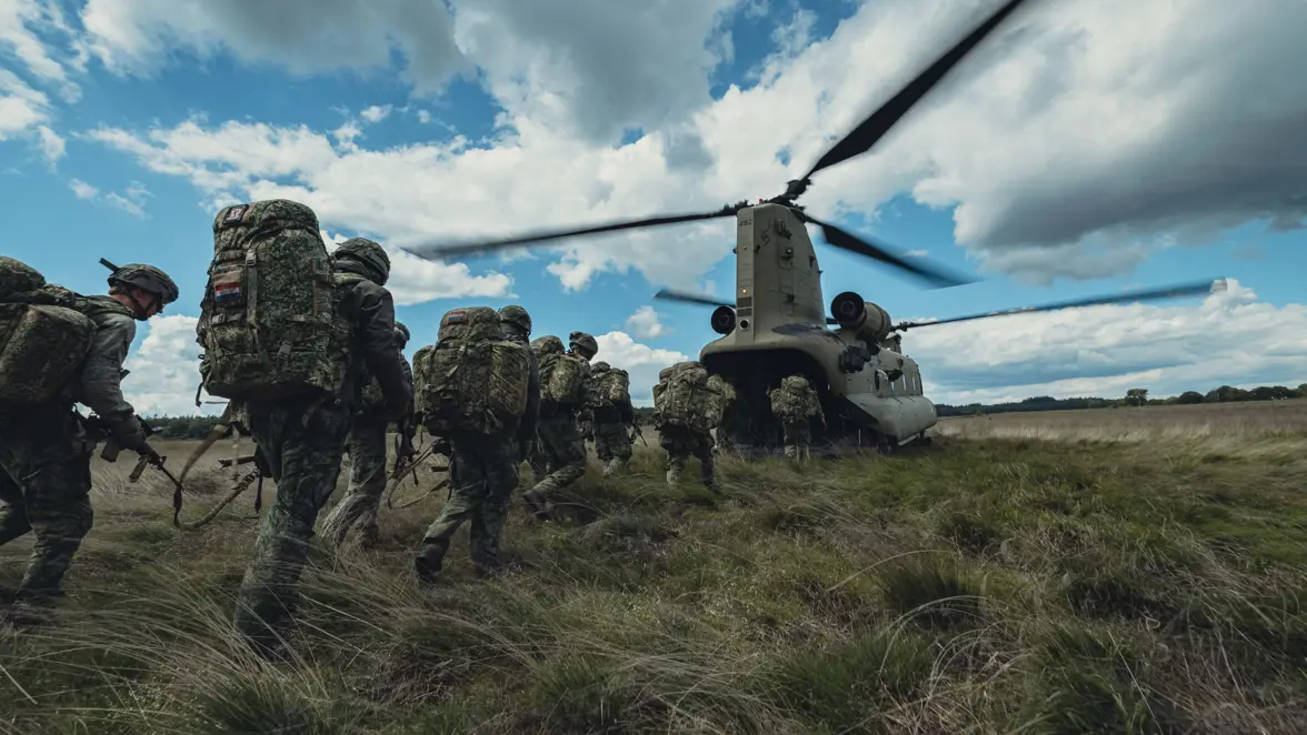 Militairen lopen achter elkaar aan over de heide naar de achterklep van de Chinook en stappen in de helikopter.
