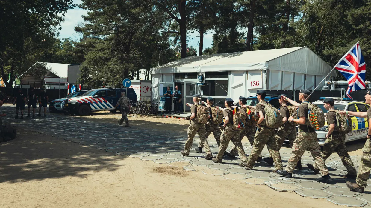 Engelse militairen lopen kamp Heumensoord op, in de verte een voertuig van de Koninklijke Marechaussee.