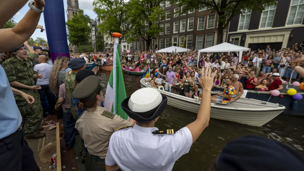 Militairen wuiven naar de menigte aan een kant van de gracht.