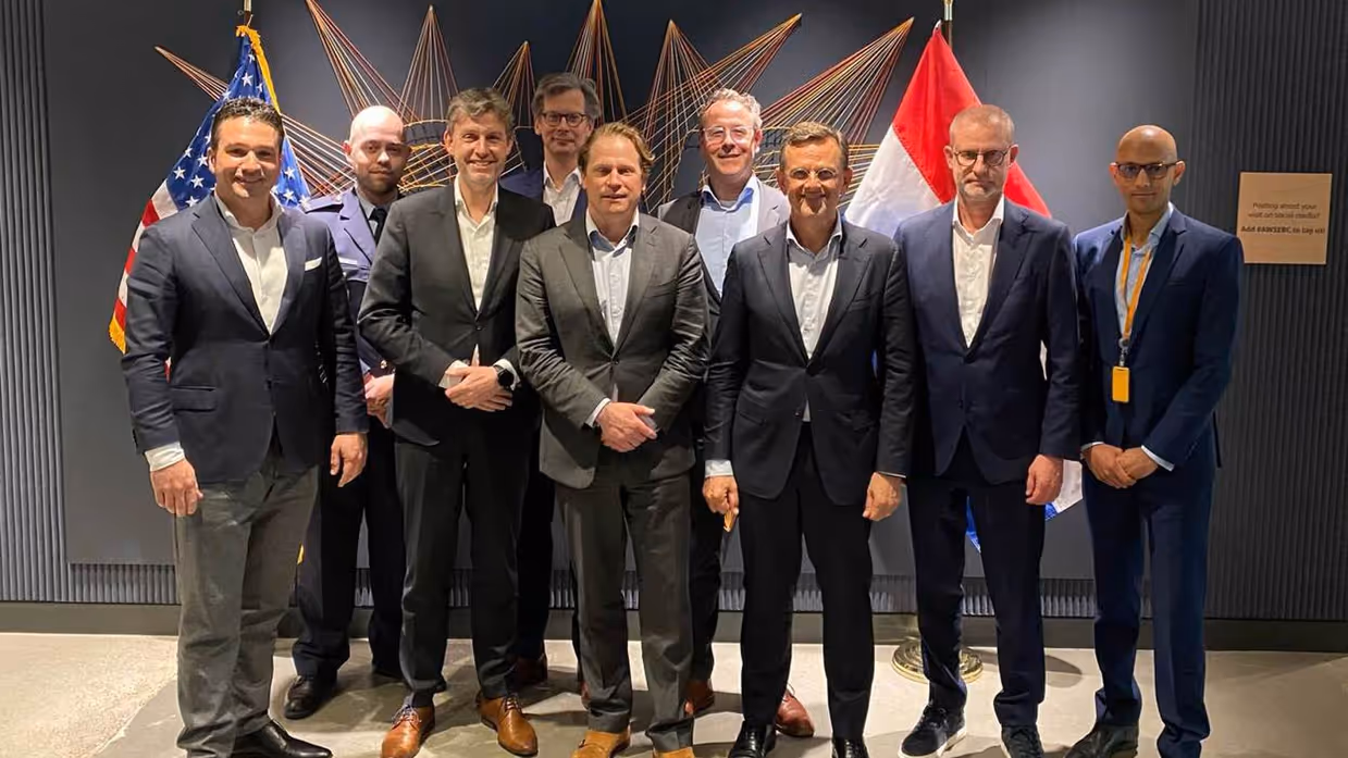 Groep mannen poseert in pak voor Nederlandse en Amerikaanse vlag.