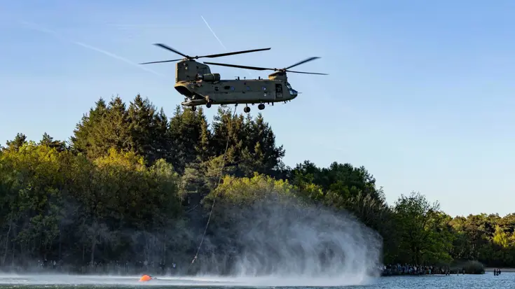 Een helikopter vult de waterzak die eronder hangt. 