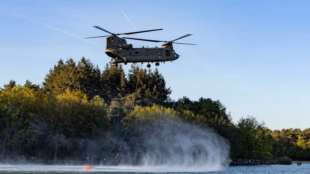Een helikopter met bluszak hangt boven het water.
