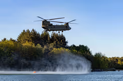 Een helikopter met bluszak hangt boven het water.