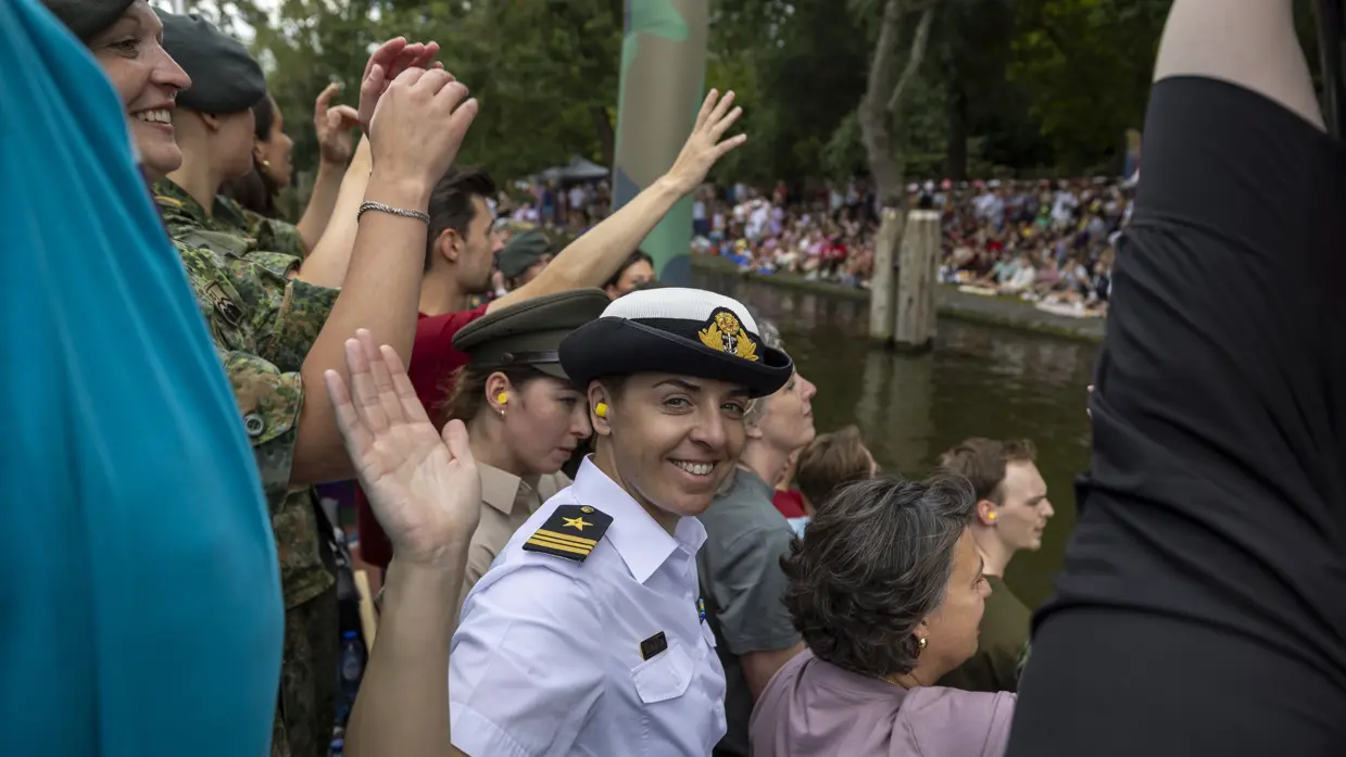 Militairen wuiven vanaf een bootje naar alle mensen om hen heen.