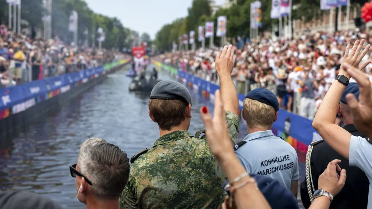 In de voorgrond wuiven militairen vanaf een bootje naar de menigte op de kanten naast de gracht.