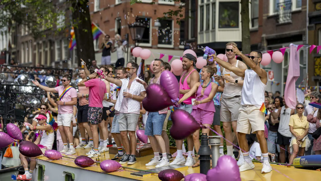 Een groep mensen kijkt feestelijk toe op de passerende bootjes.