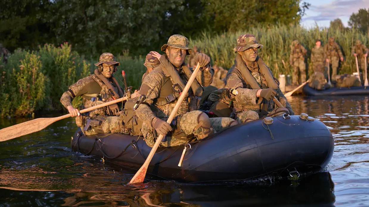 Mariniers roeien met rubberboten over een watertje.