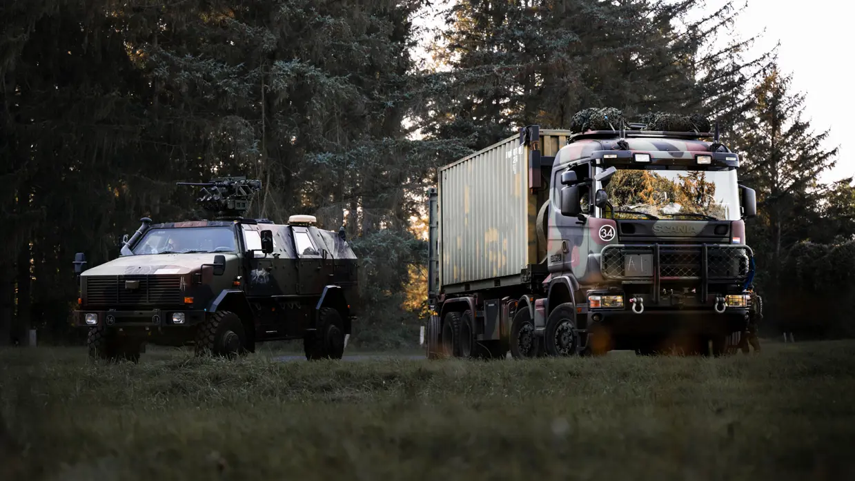Een pantservoertuig en een vrachtwagen voor de bosrand.  