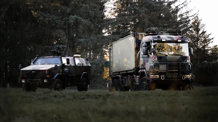 Een pantservoertuig en een vrachtwagen voor de bosrand.  