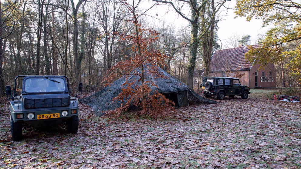 Legertent in bos met aan beide kanten een jeep.