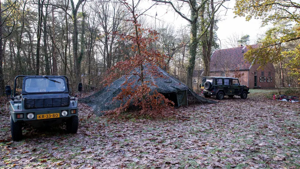 Legertent in bos met aan beide kanten een jeep.