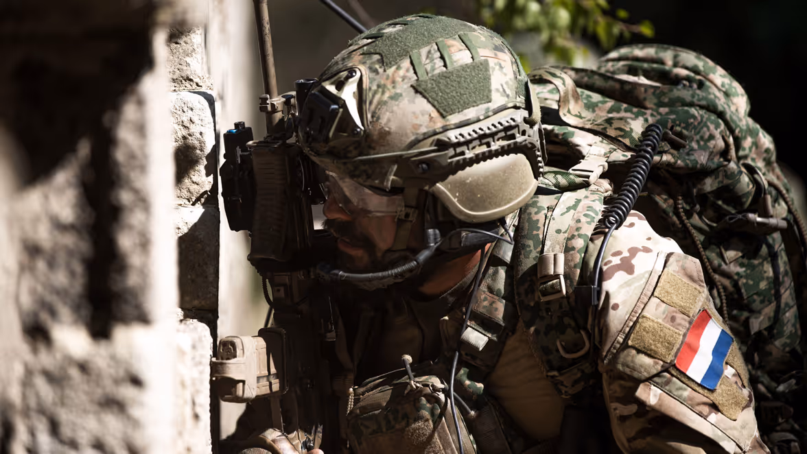 Militair kijkt om hoek van gebouw.