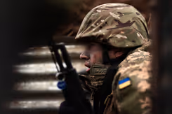 Oekraïense militair zit gehurkt met wapen voor zich.