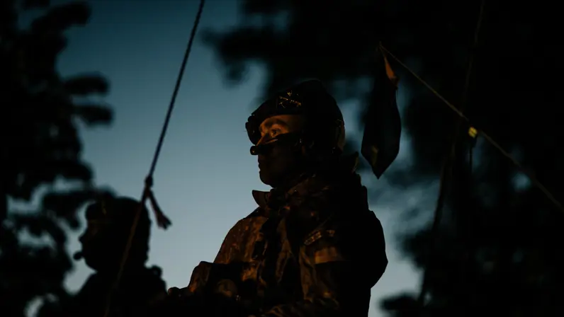Het is donker. Er is een silhouet te zien van een militair die bovenluiks zit.