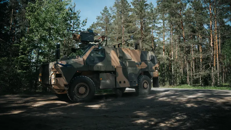 Een defensievoertuig van het type Bushmaster in het bos, die afslaat richting de camera