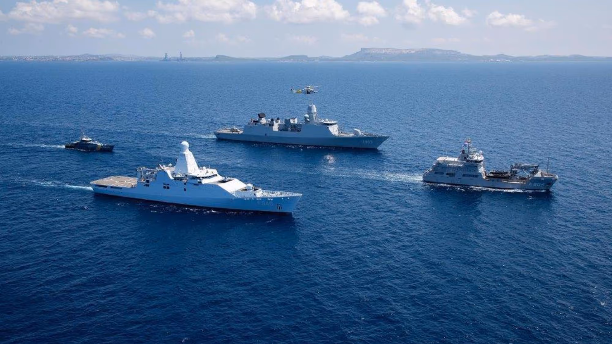 4 marineschepen varen in een ruitvorm op het water.