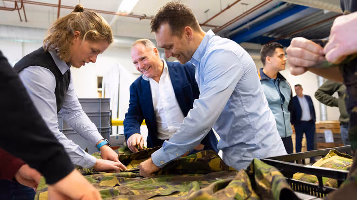 Medewerkers van het DJI raken de militaire uniformen aan, die op een glimmende tafel liggen.