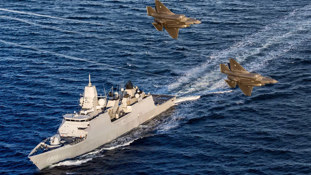Zr.Ms. Tromp vaart op zee terwijl 2 gevechtsvliegtuigen er overheen vliegen.