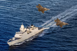 Zr.Ms. Tromp vaart op zee terwijl 2 gevechtsvliegtuigen er overheen vliegen.