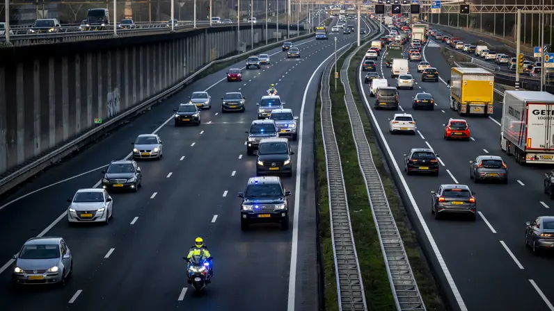 Een motorbegeleider van de Koninklijke Marechaussee rijdt voor een colonne dienstvoertuigen over de snelweg.