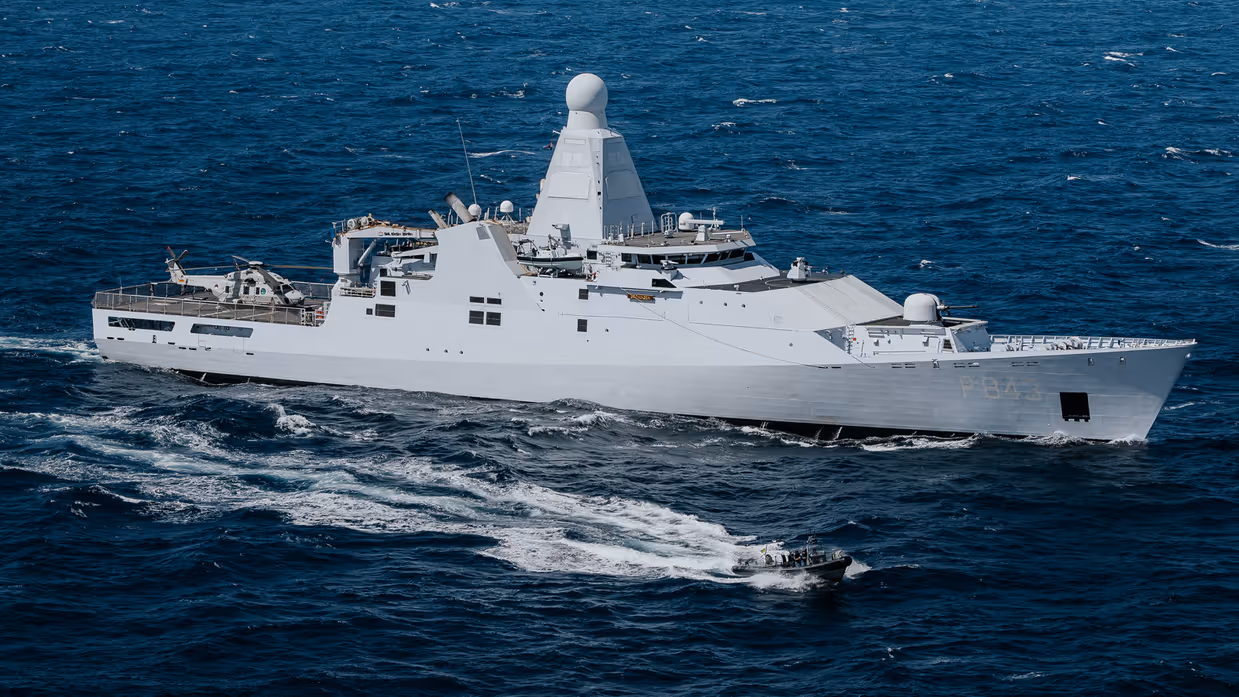 Marineschip met klein bootje varen naast elkaar.