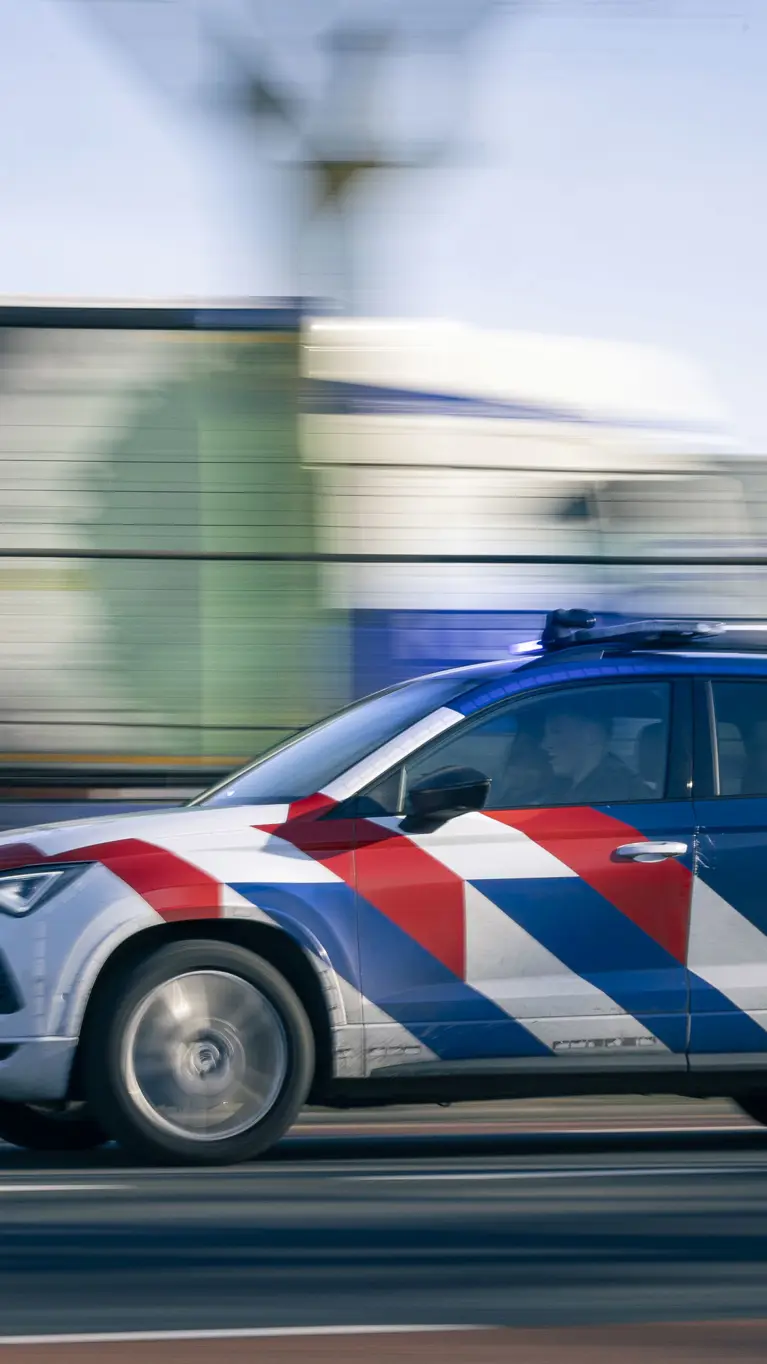 Een dienstvoertuig met zwaailicht dat snel langs een vangrail rijdt.
