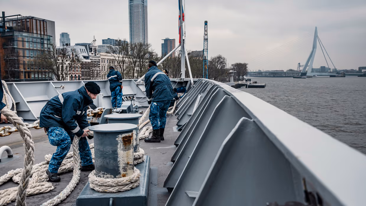 Marinepersoneel op dek aan het werk, met op achtergrond Erasmusbrug.