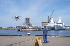 Militair staat op kade en kijkt naar drone die opstijgt.