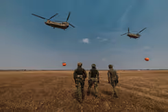 Militairen op de rug gezien. In de lucht 2 helikopters met waterzakken.