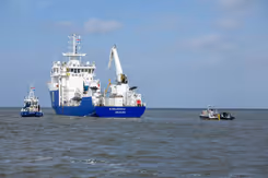 Het schip de NS Geosea, van de onderkant blauw en de bovenkant wit, vaart op zee. Links en rechts een klein bootje.
