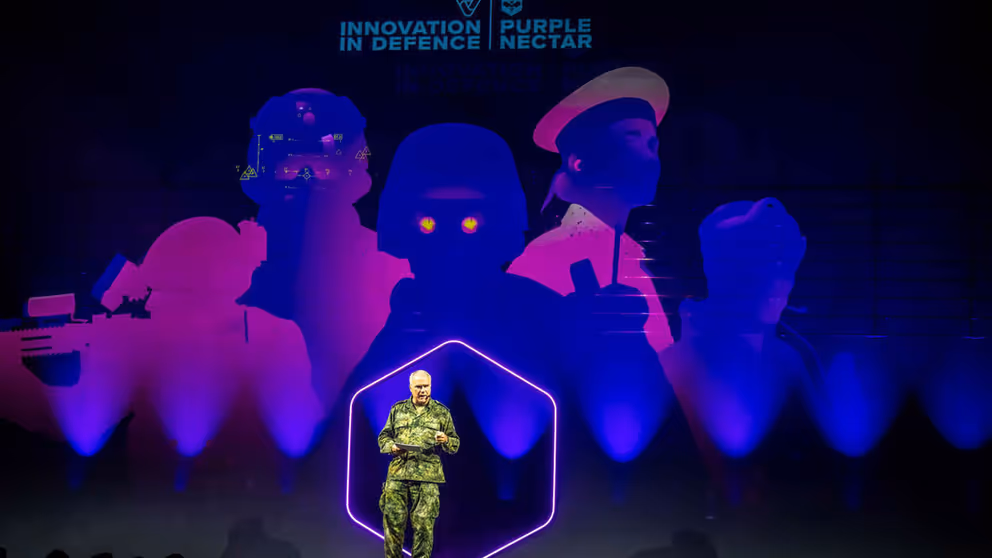 Generaal Eichelsheim staat op podium tegen blauwpaarse achtergrond.