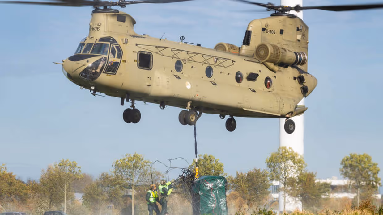 Hulpverleners hangen lading onder aan een Chinook die in de lucht hangt.