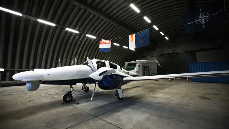 Nieuwe vliegtuig van de Marechaussee in een hangar met de Nederlandse vlag en vlag met logo van de KMar er boven.