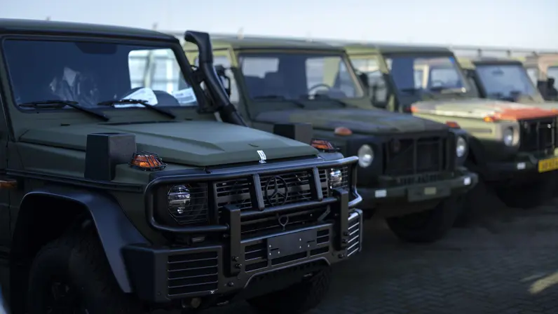 Een zijaanzicht van een Wolf GWT op de voorgrond en daarachter een rijtje verouderde MB’s. 