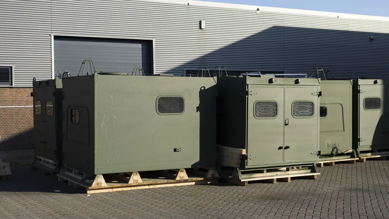 Een aantal groengespoten koffers die buiten de werkplaats wachten op montage.    