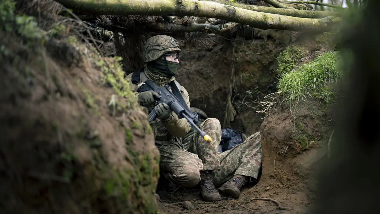 Een Oekraïense militair met een geweer in zijn hand, kijkt gespannen naar buiten vanuit een loopgraaf.