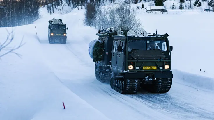 Twee rupsvoertuigen van het type BV 206 rijden over een besneeuwde weg.