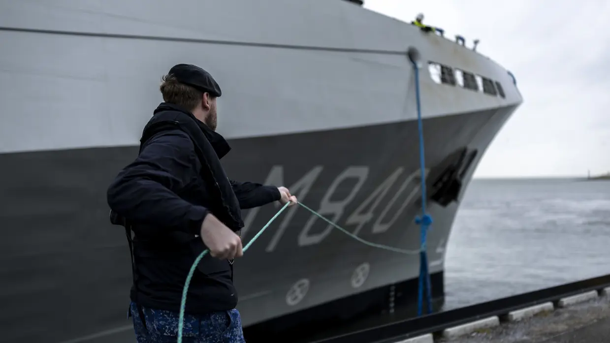 Een militair van de marine haalt met een touw een van de trossen binnen.