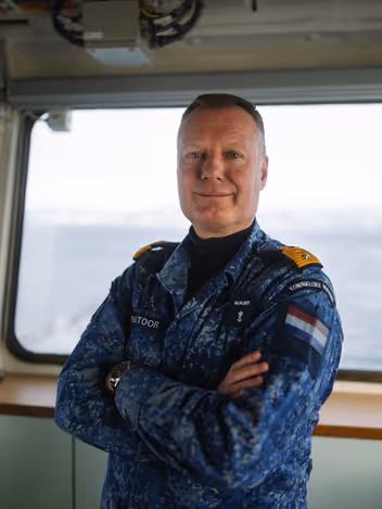 Commandeur Pastoor in maritiem camouflage-uniform aan boord van een marineschip. 