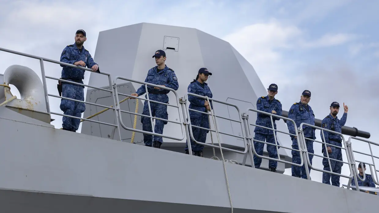 Bemanningsleden bij de reling, met het scheepskanon op de achtergrond. 