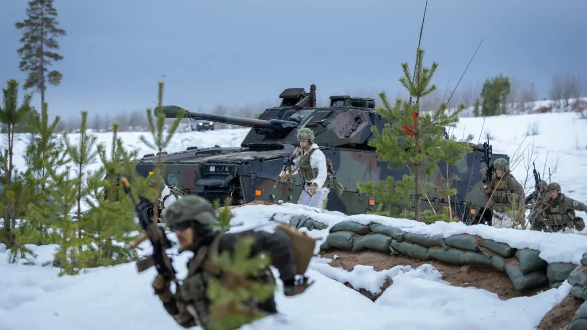 Een CV90 in een winters landschap brengt manschappen naar de rand van een loopgraaf.