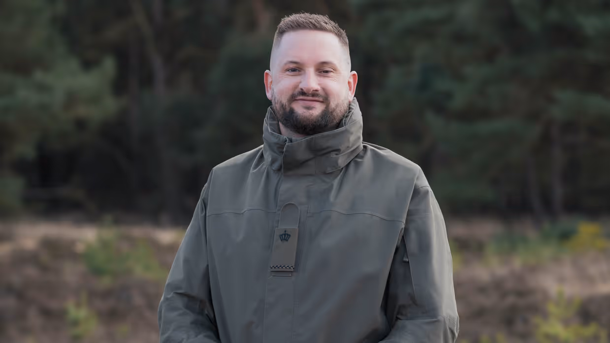 Een militair poseert met handen over elkaar op de hei.